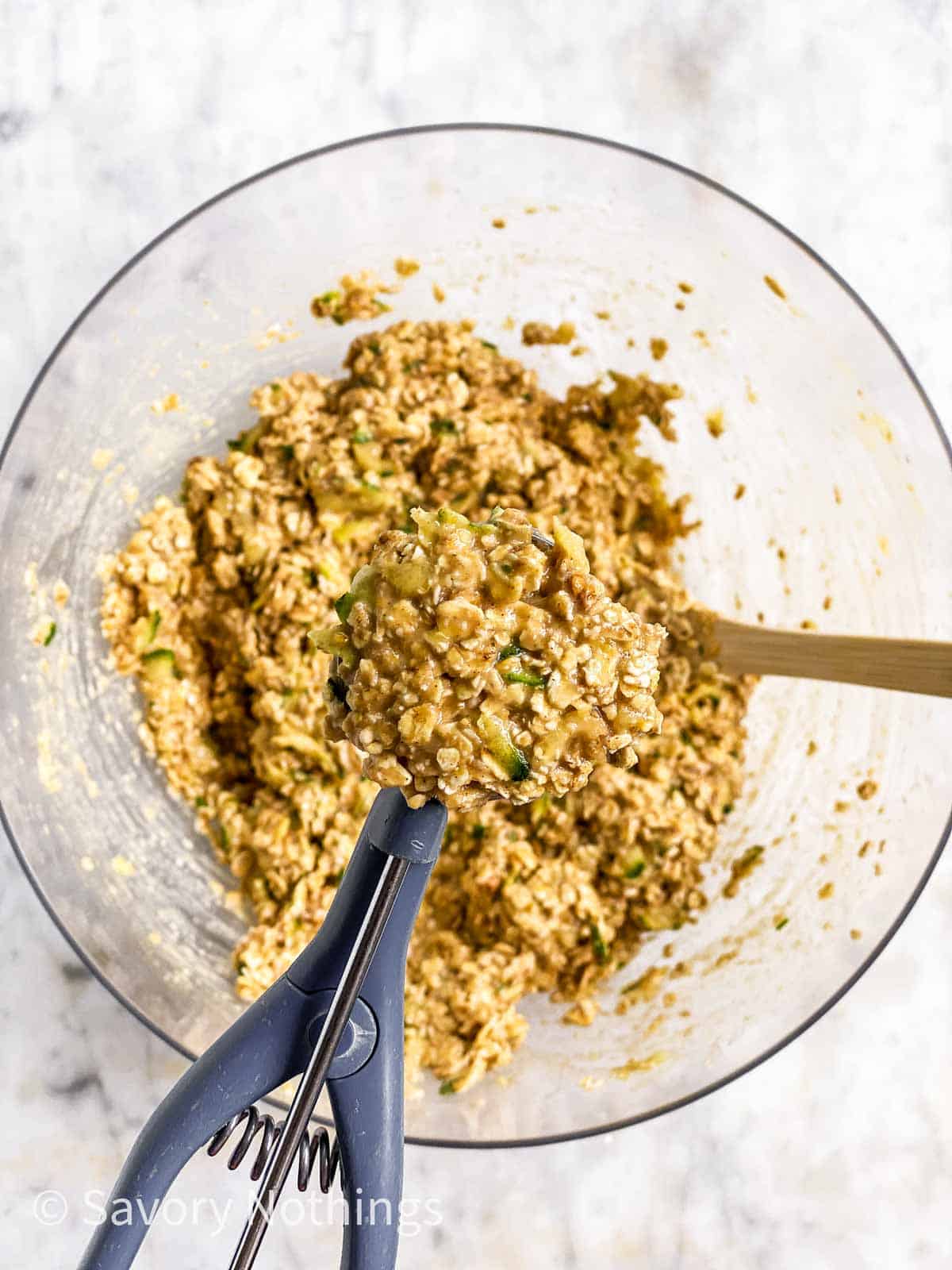 cookie scoop filled with zucchini breakfast cookie dough over glass bowl with cookie dough