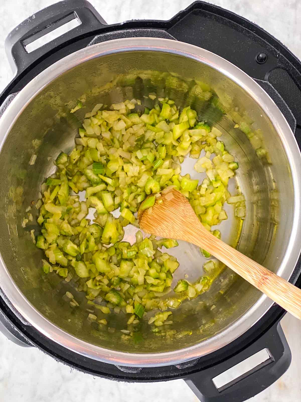 Sautéed onion and celery in instant pot with wooden spoon stirring