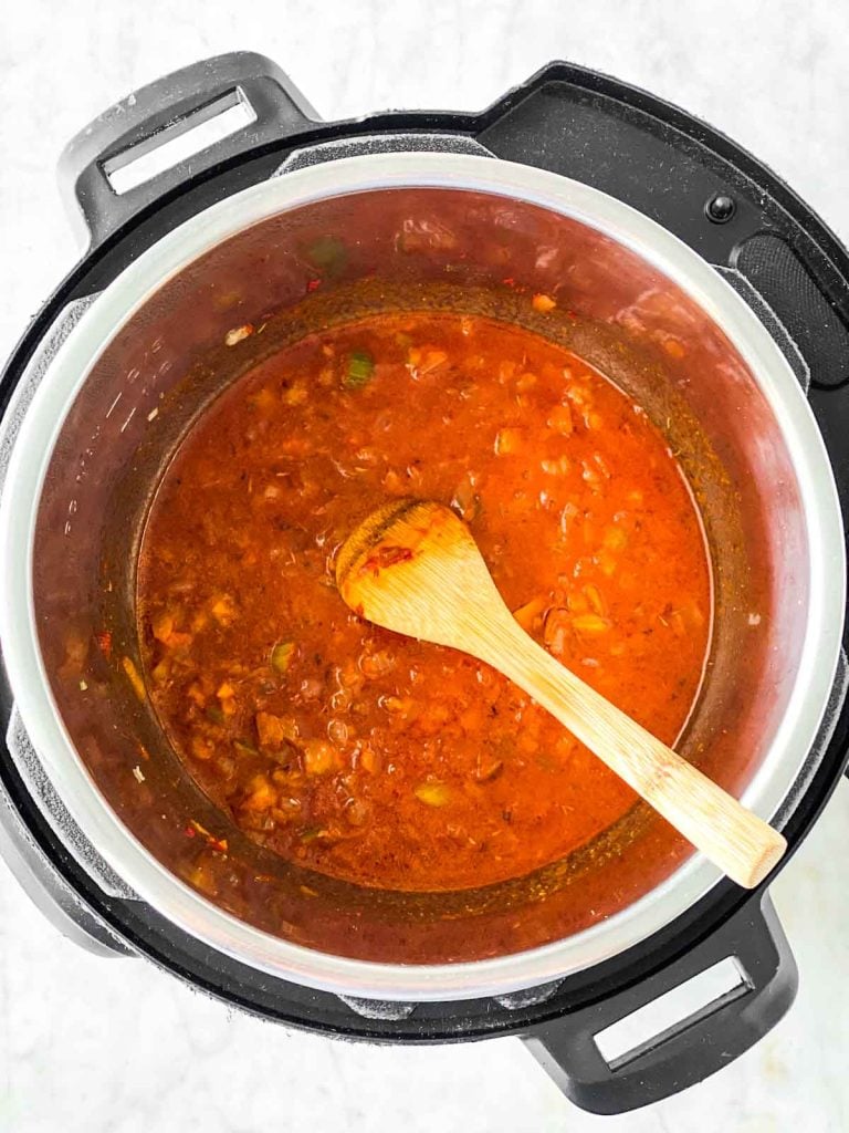 Wooden spoon scraping browned bits off bottom of instant pot filled with tomato sauce