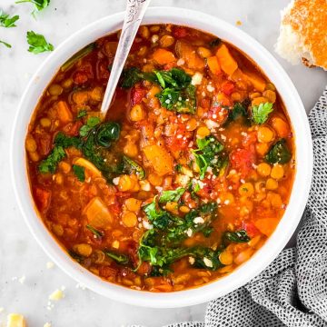 Overhead view of lentil soup in white bowl garnished with parsley and Parmesan cheese