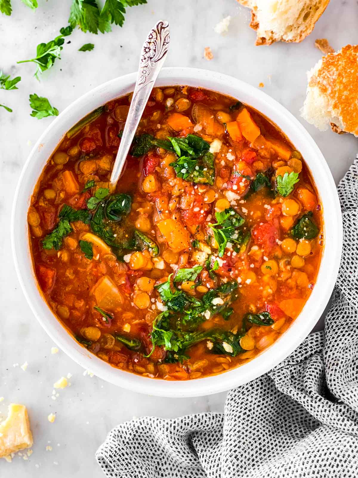 Overhead view of lentil soup in white bowl garnished with parsley and Parmesan cheese