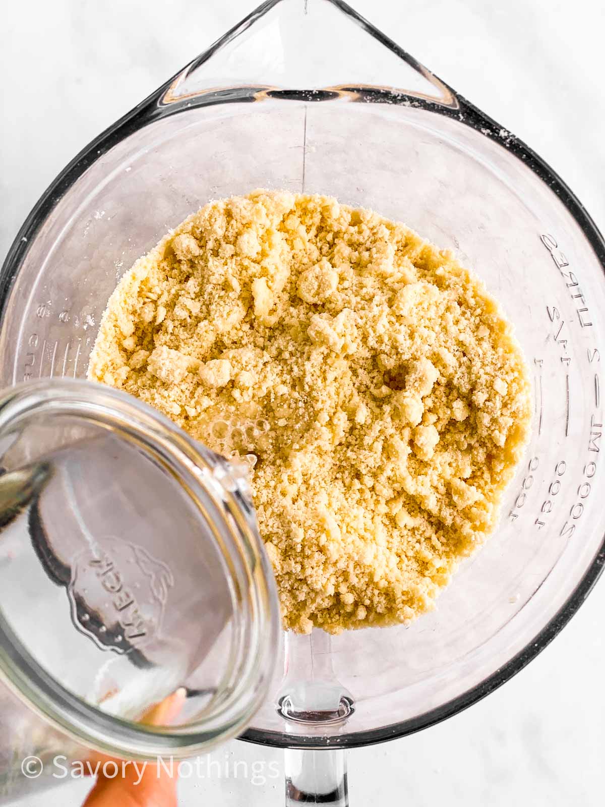 water pouring from glass measuring jug into bowl with flour and butter crumbs