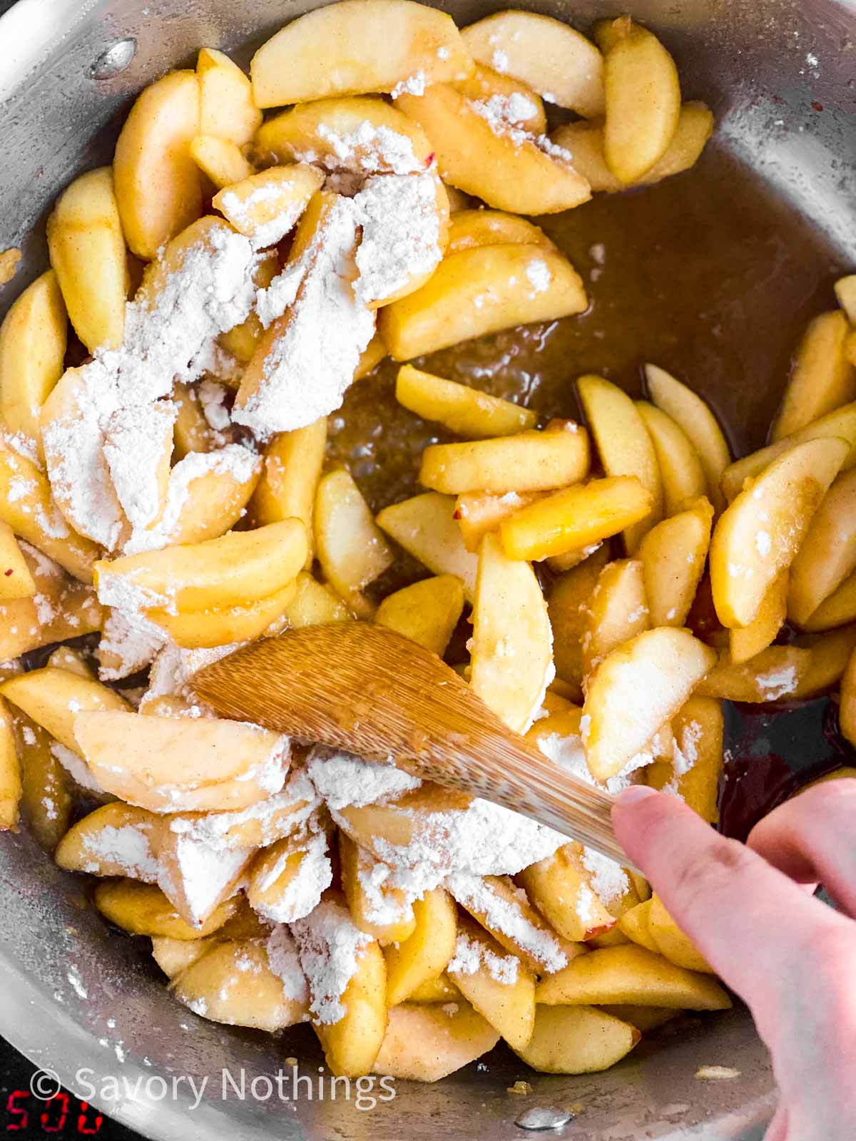 female hand stirring apple pie filling in skillet