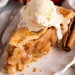 slice of apple pie topped with vanilla ice cream on white plate