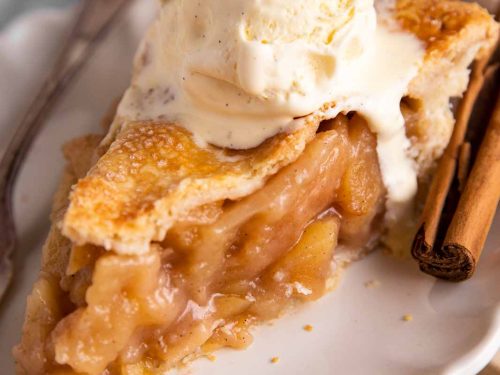 slice of apple pie topped with vanilla ice cream on white plate