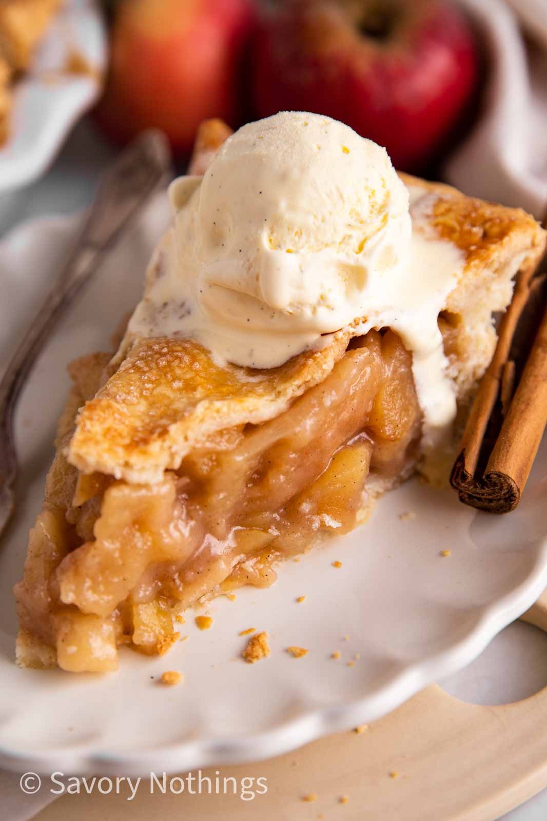 slice of apple pie topped with vanilla ice cream on white plate