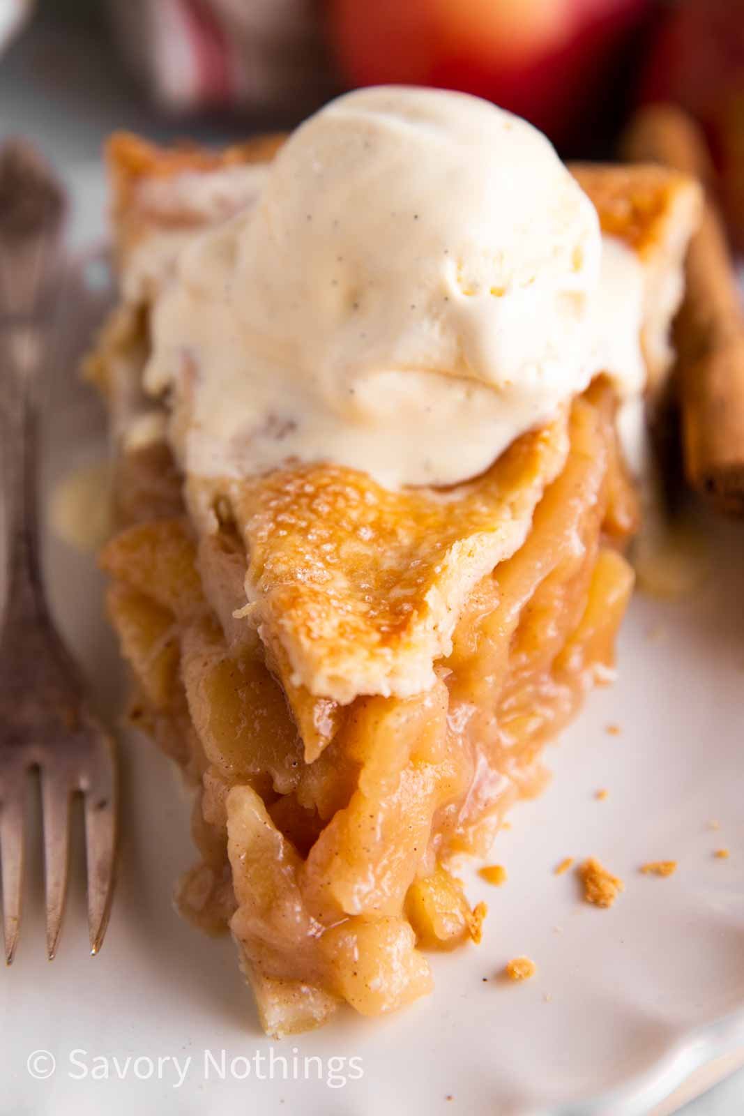 frontal view of apple pie slice on white plate garnished with vanilla ice cream