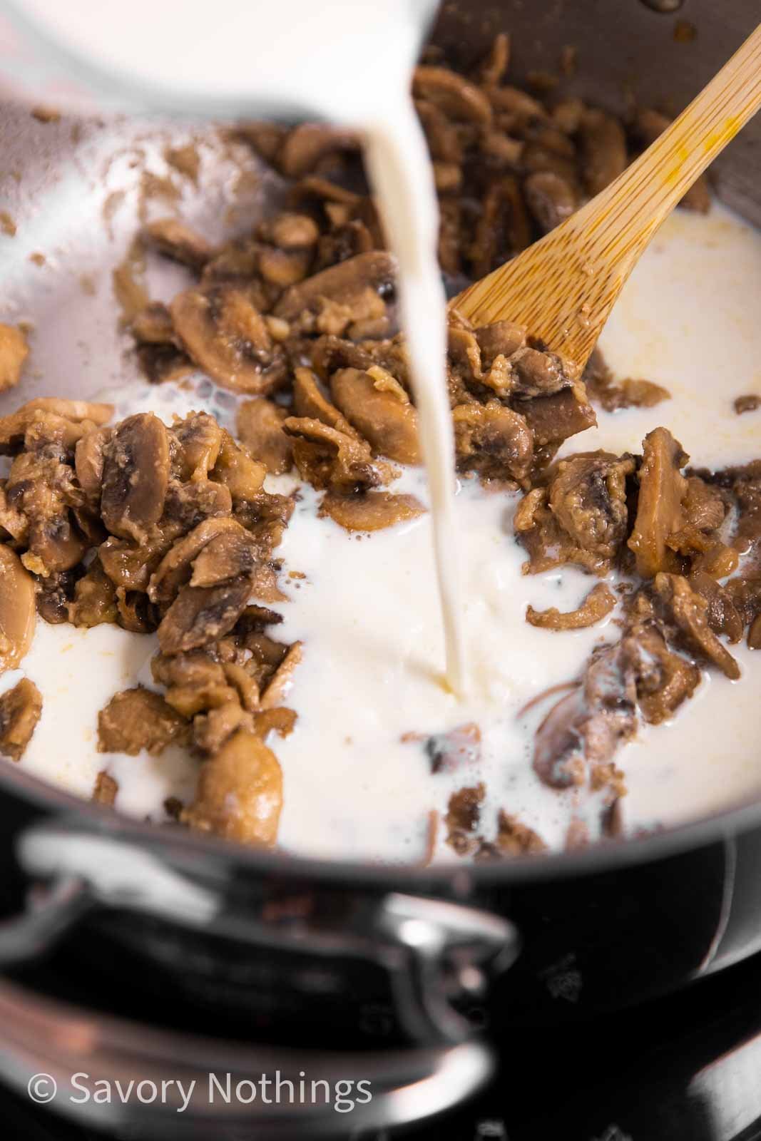 milk pouring from glass measuring jug into skillet with mushrooms