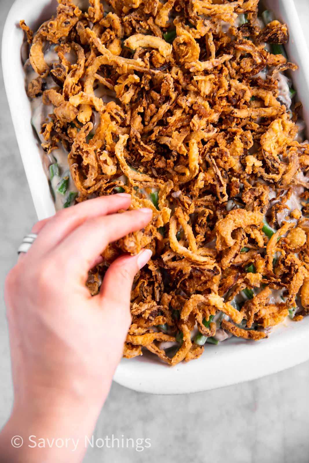 female hand sprinkling fried onions over green bean casserole