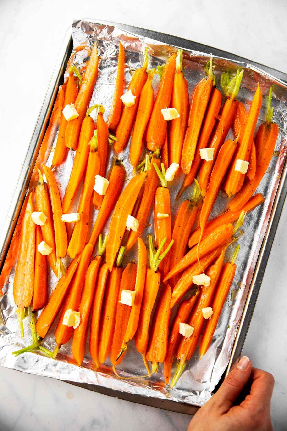 raw carrots in honey glaze dotted with butter, on foil lined pan