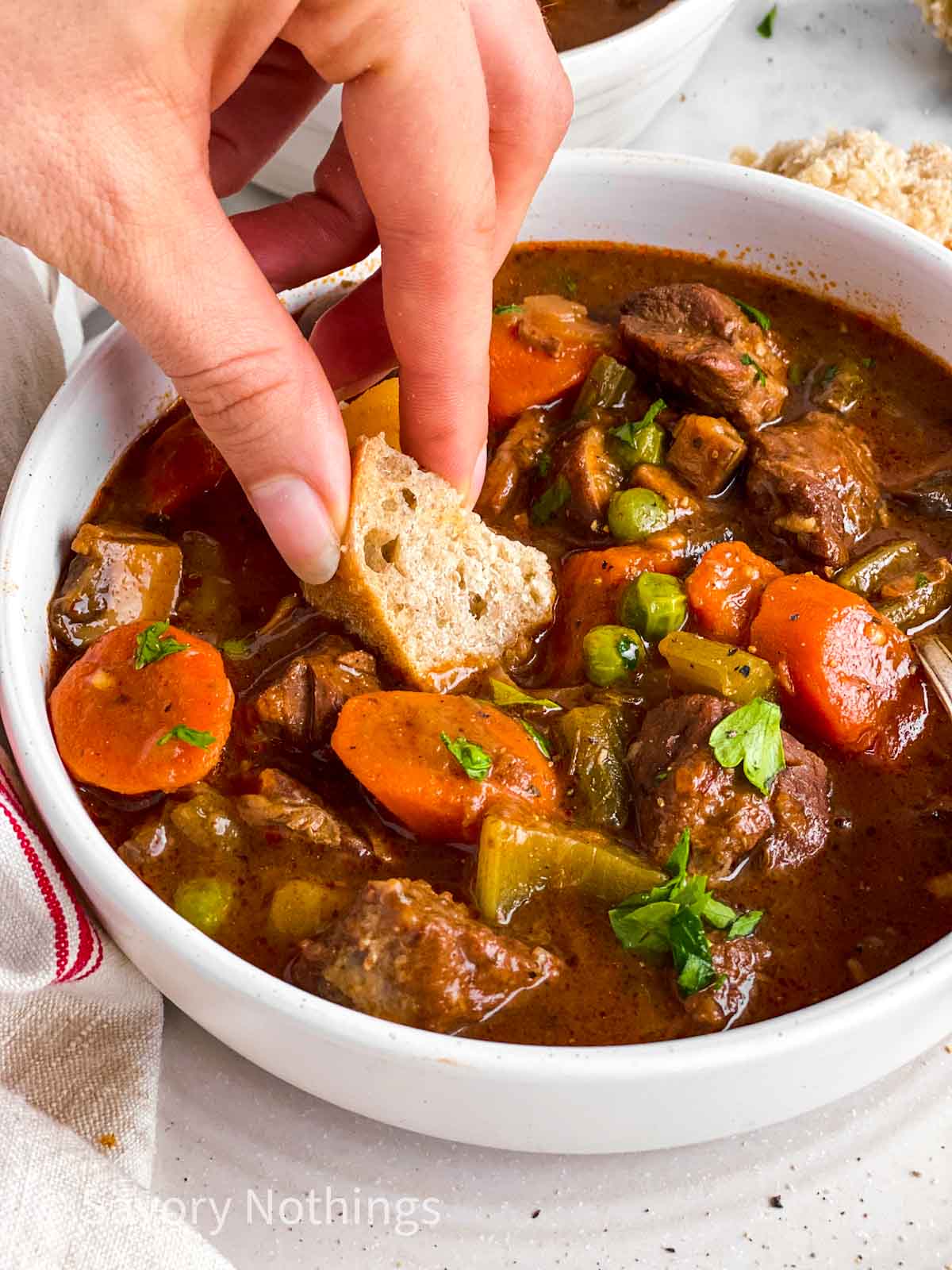 female hand dipping bread into bowl with beef stew