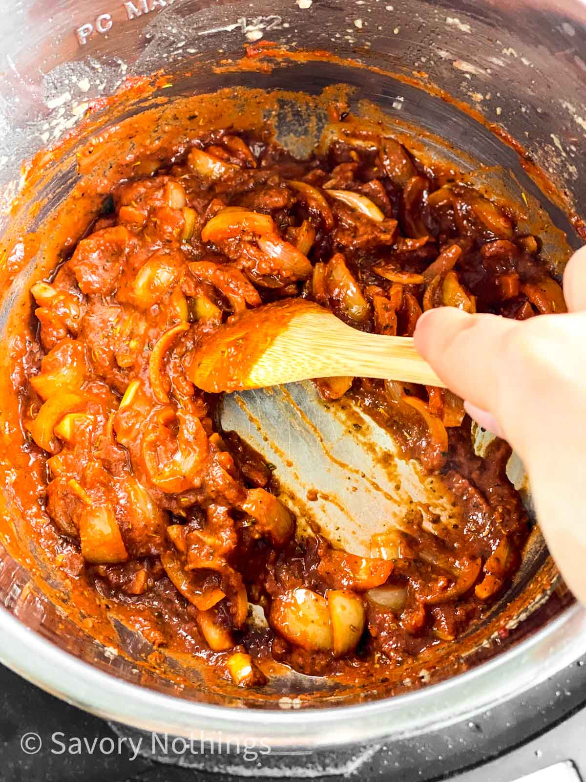 female hand using wooden spoon to scrape bottom of instant pot