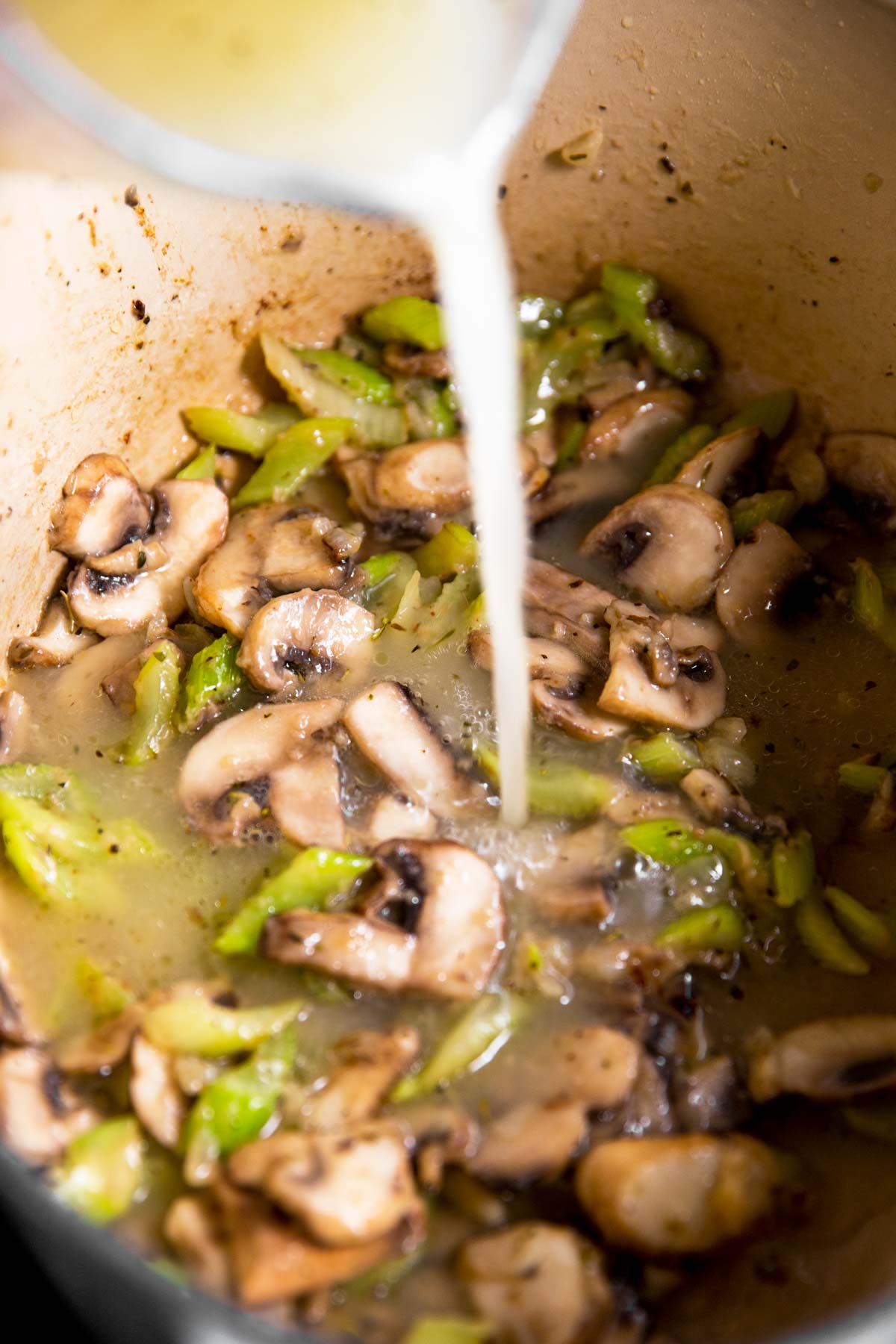 broth pouring from glass measuring jug into Dutch oven with vegetables