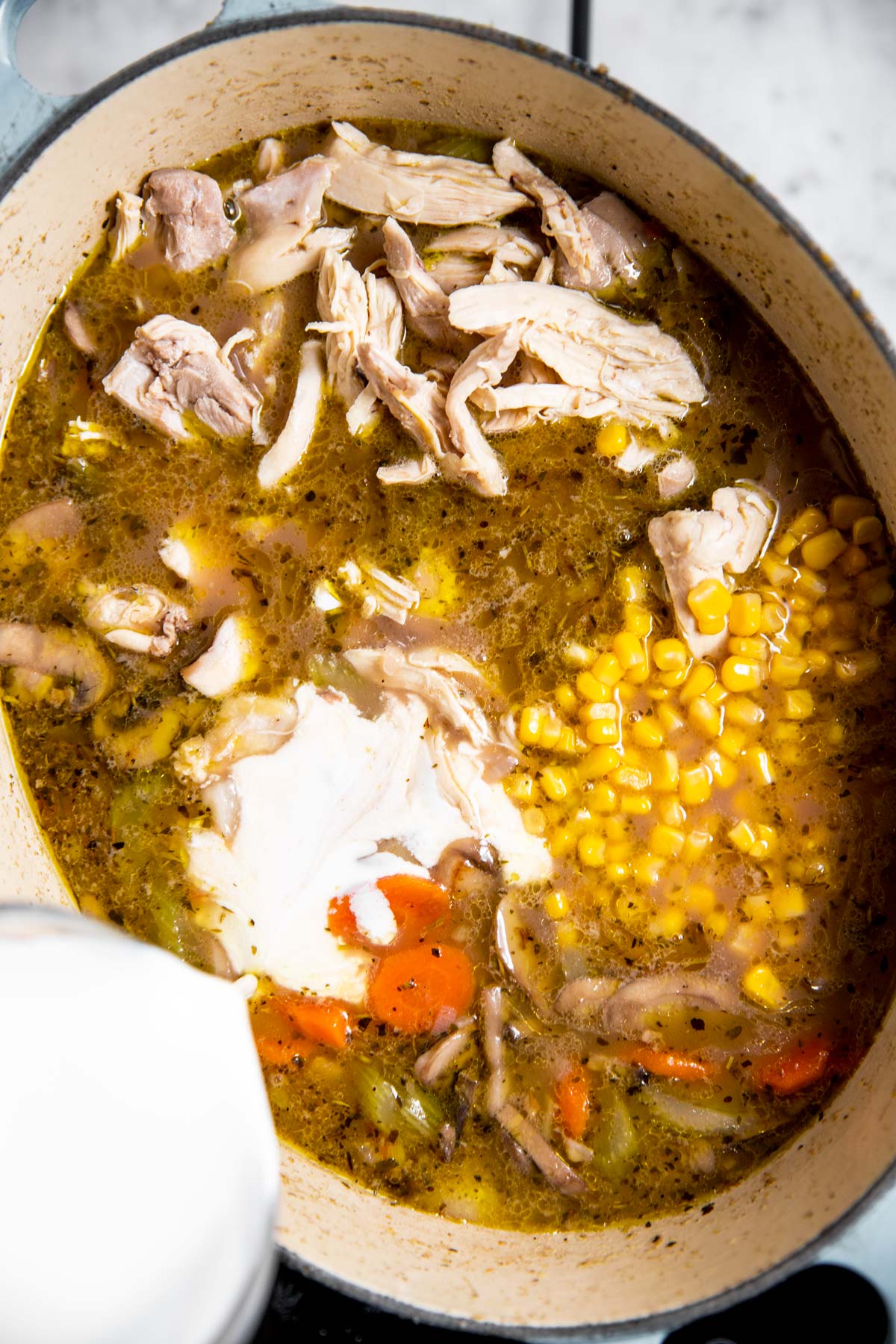 half and half pouring from glass measuring jug into pot of turkey soup