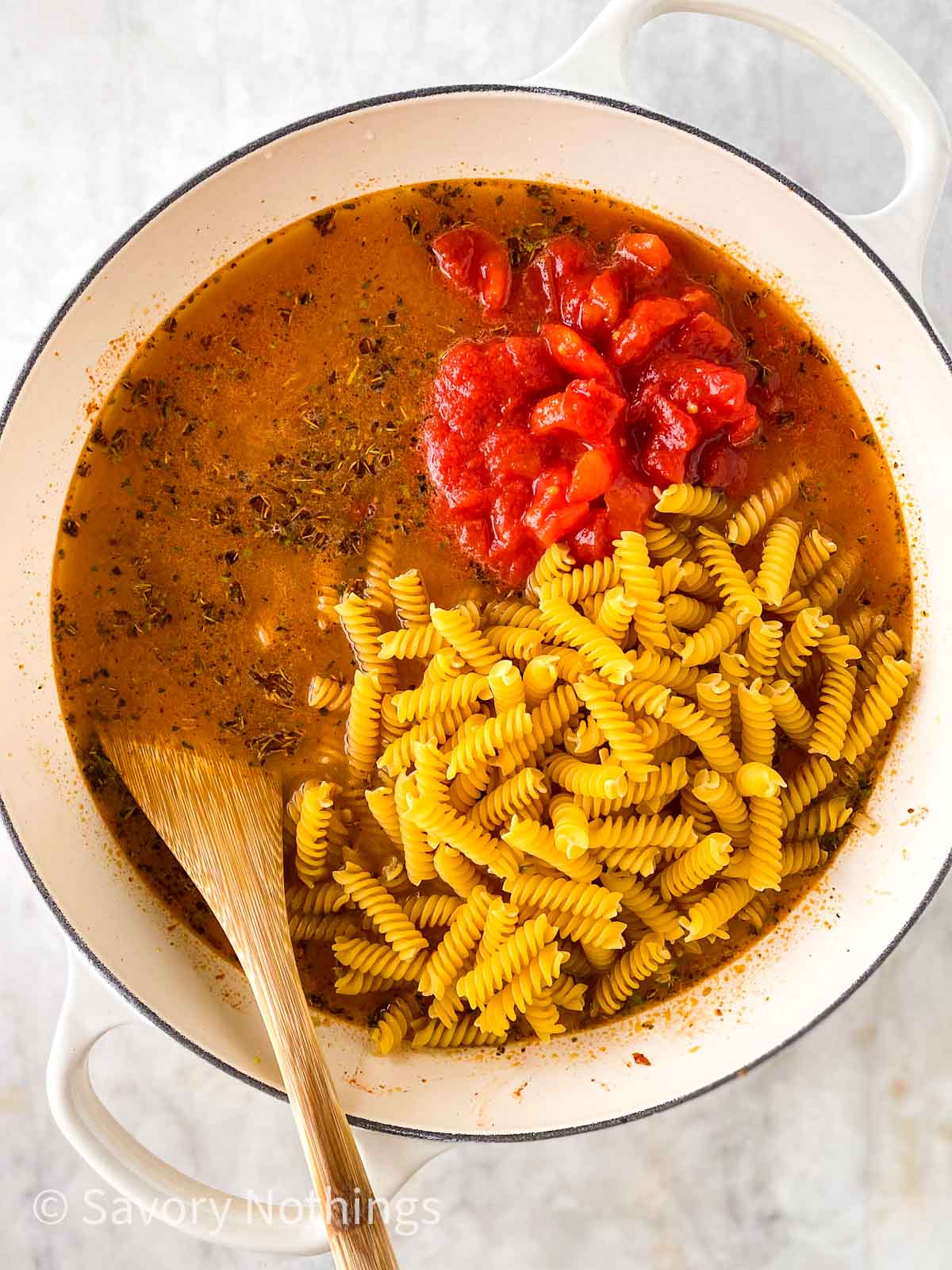 broth, dry pasta and diced tomatoes in white cast iron skillet