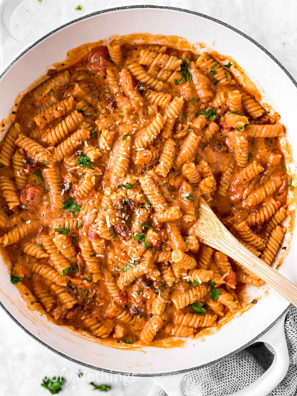 creamy tomato pasta in white dutch oven with wooden spoon stuck inside