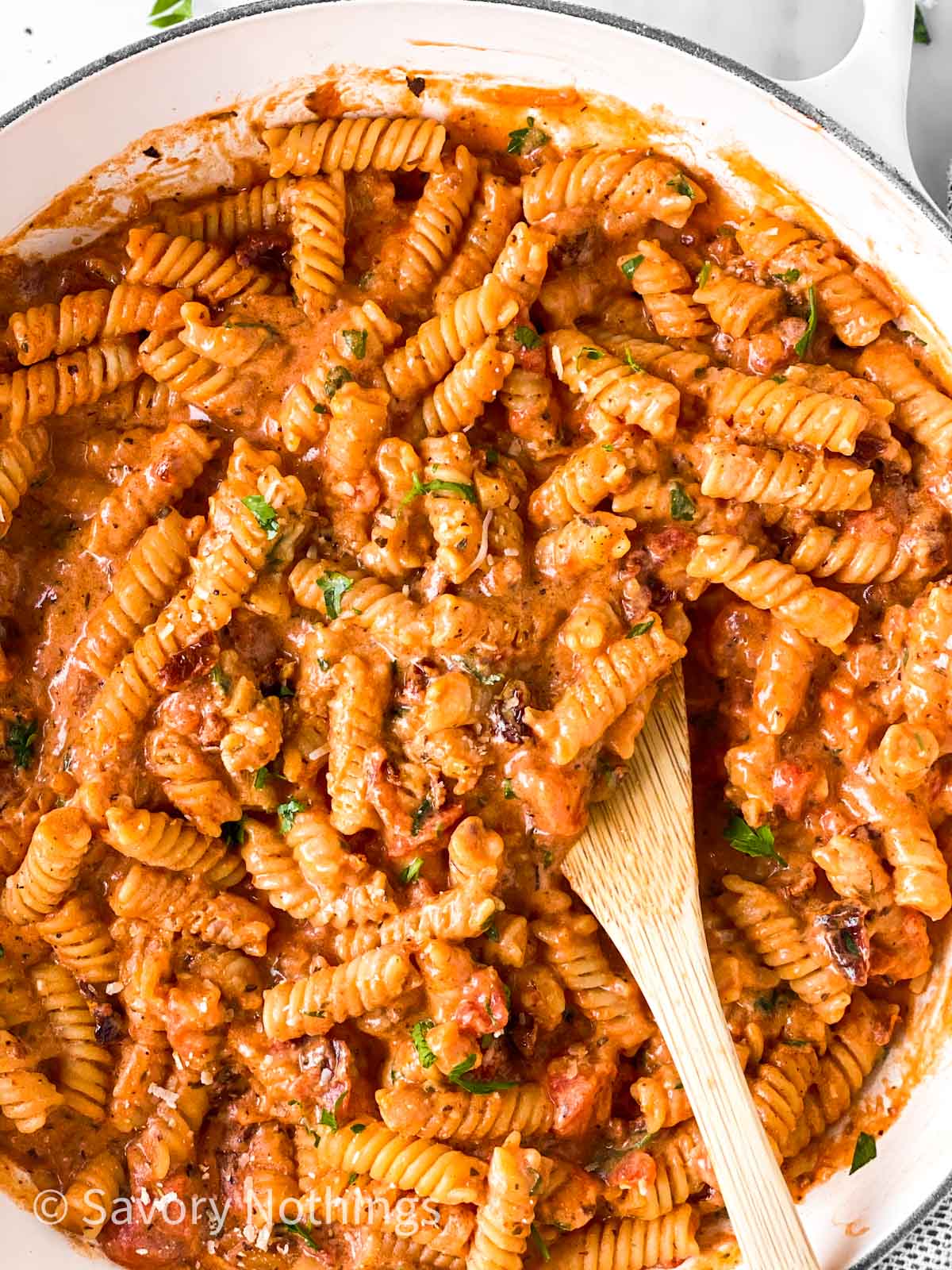 close up photo of wooden spoon in a pot of creamy tomato pasta