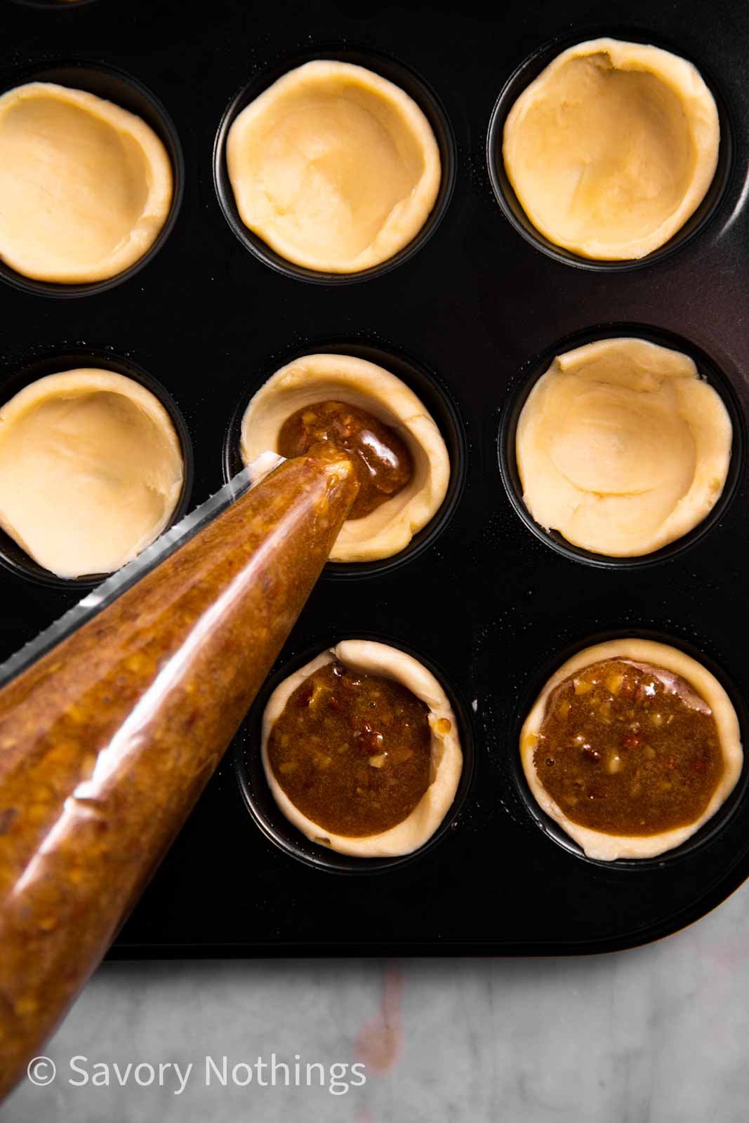 pecan pie filling piping from plastic piping bag into miniature pie shells in muffin pan