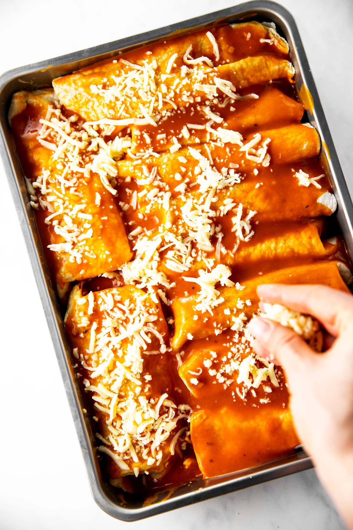 female hand sprinkling cheese over pan filled with turkey enchiladas