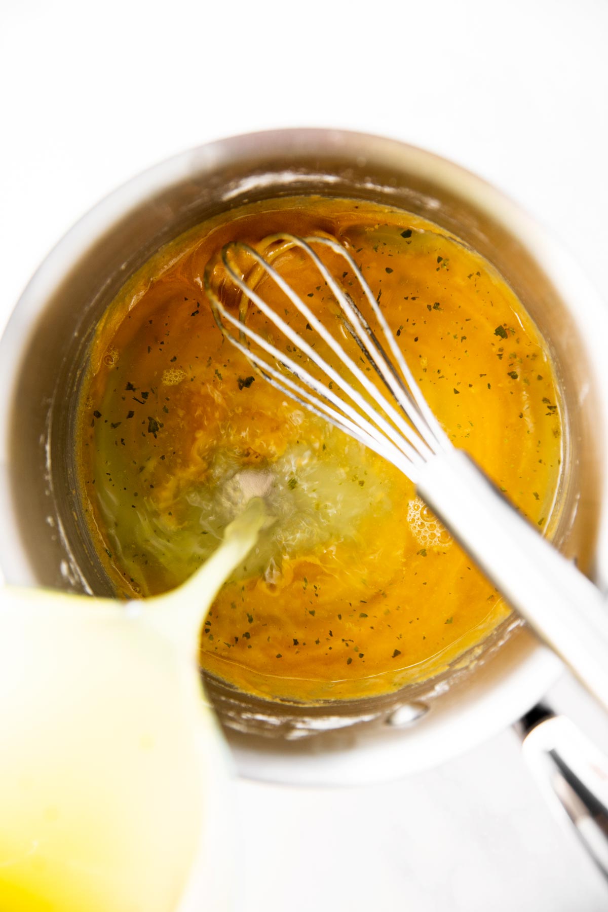 broth pouring from glass measuring jug into saucepan with roux