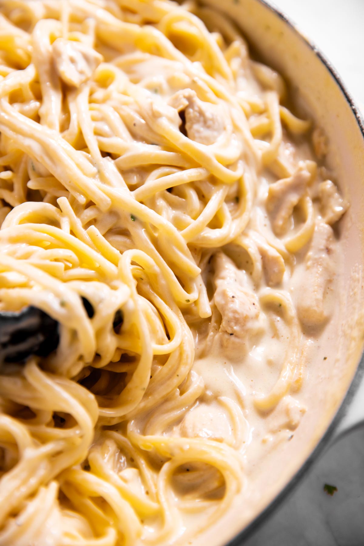 close up photo of kitchen tongs stuck in pan with chicken fettuccine alfredo