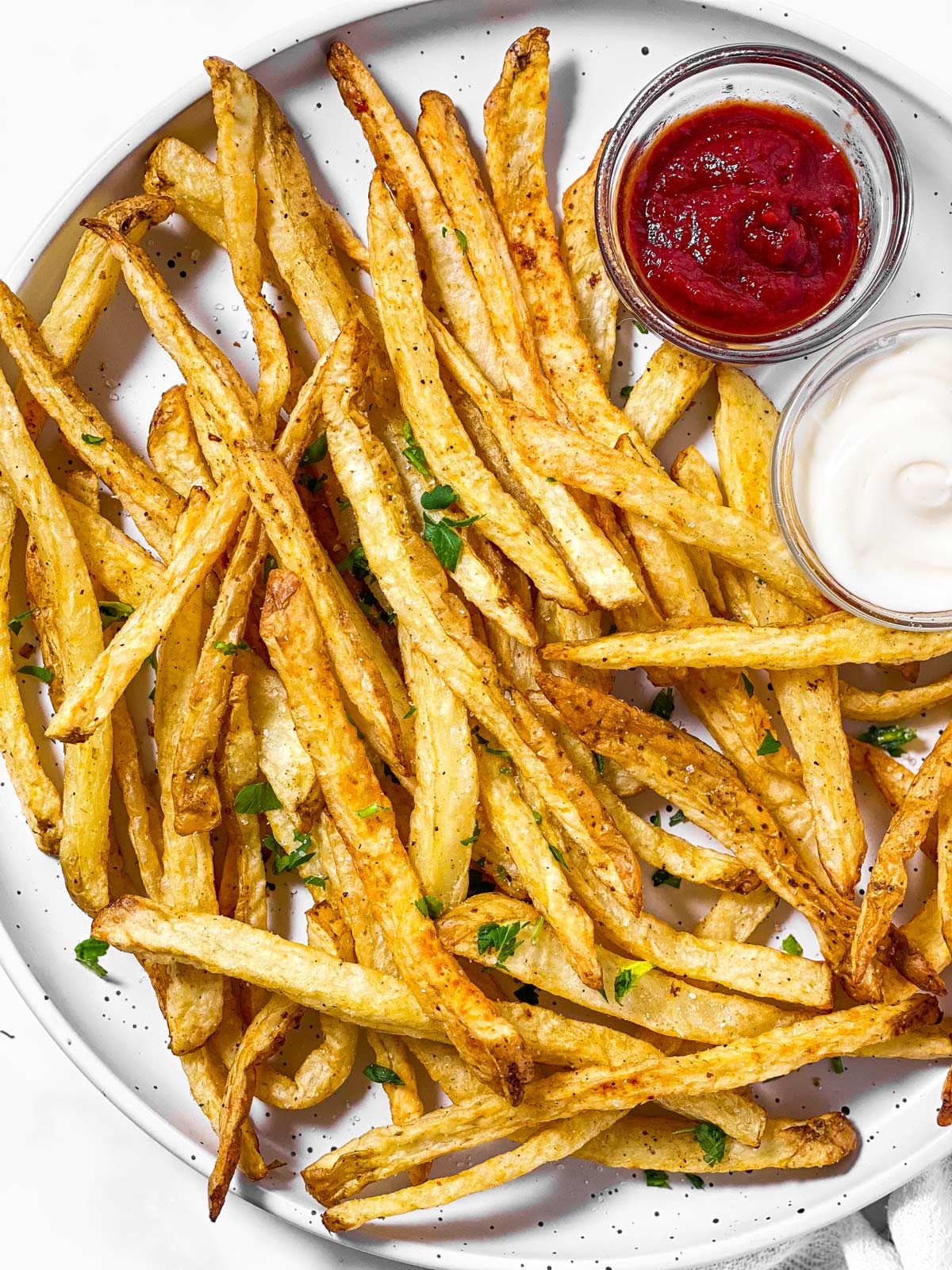 overhead close up view of french fries on white plate with small bowls of ketchup and mayonnaise