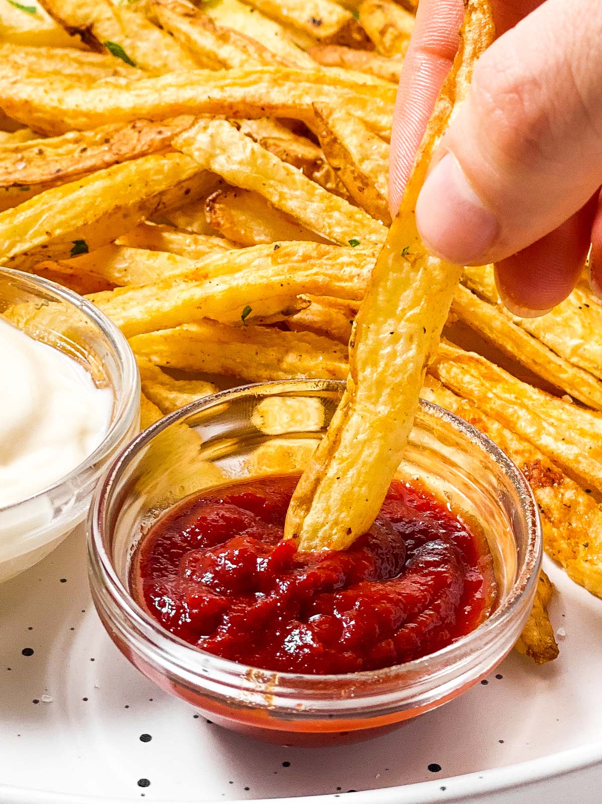 female hand dipping air fried french fry in small bowl with ketchup