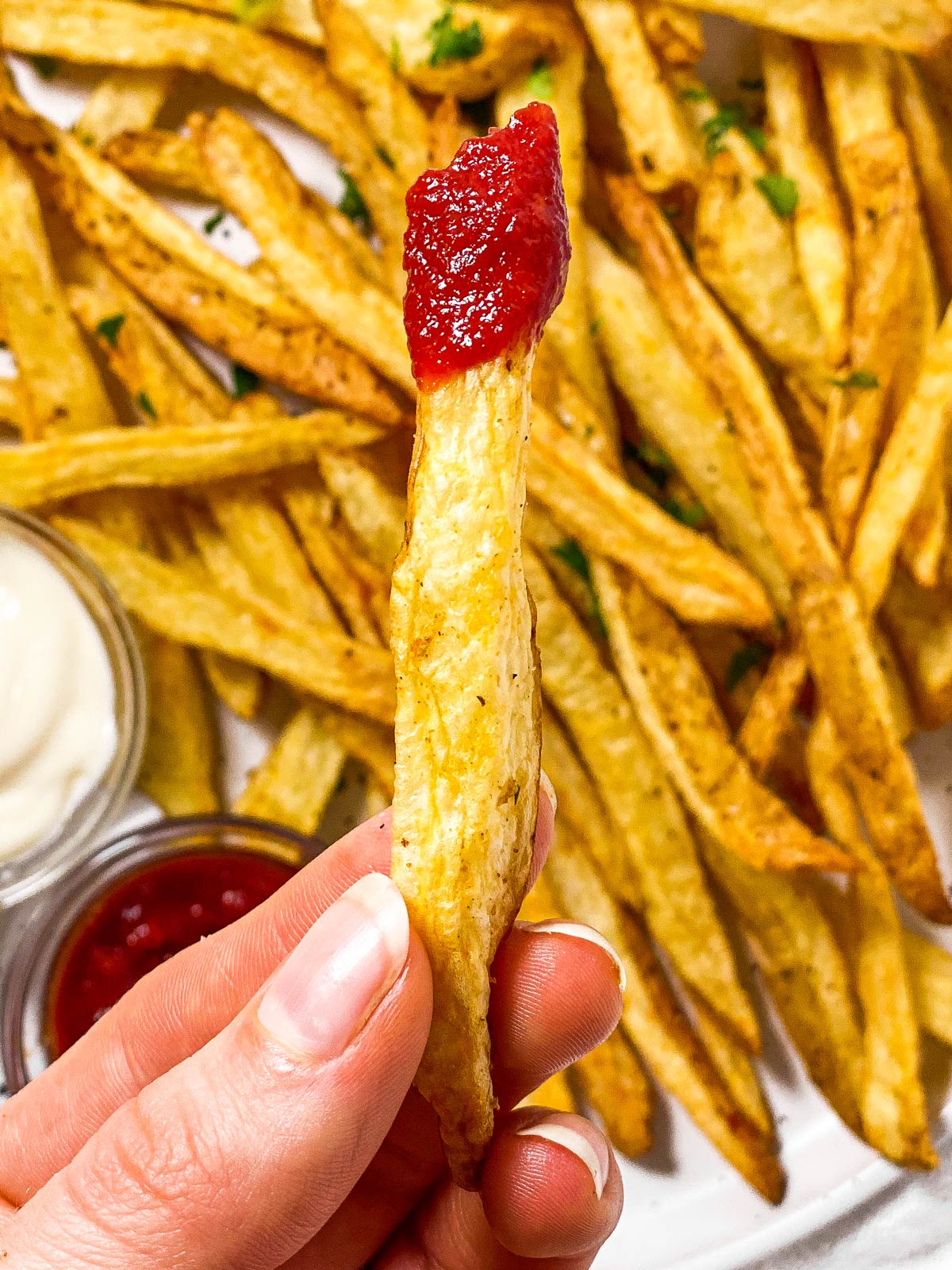 female hand holding french fry with ketchup