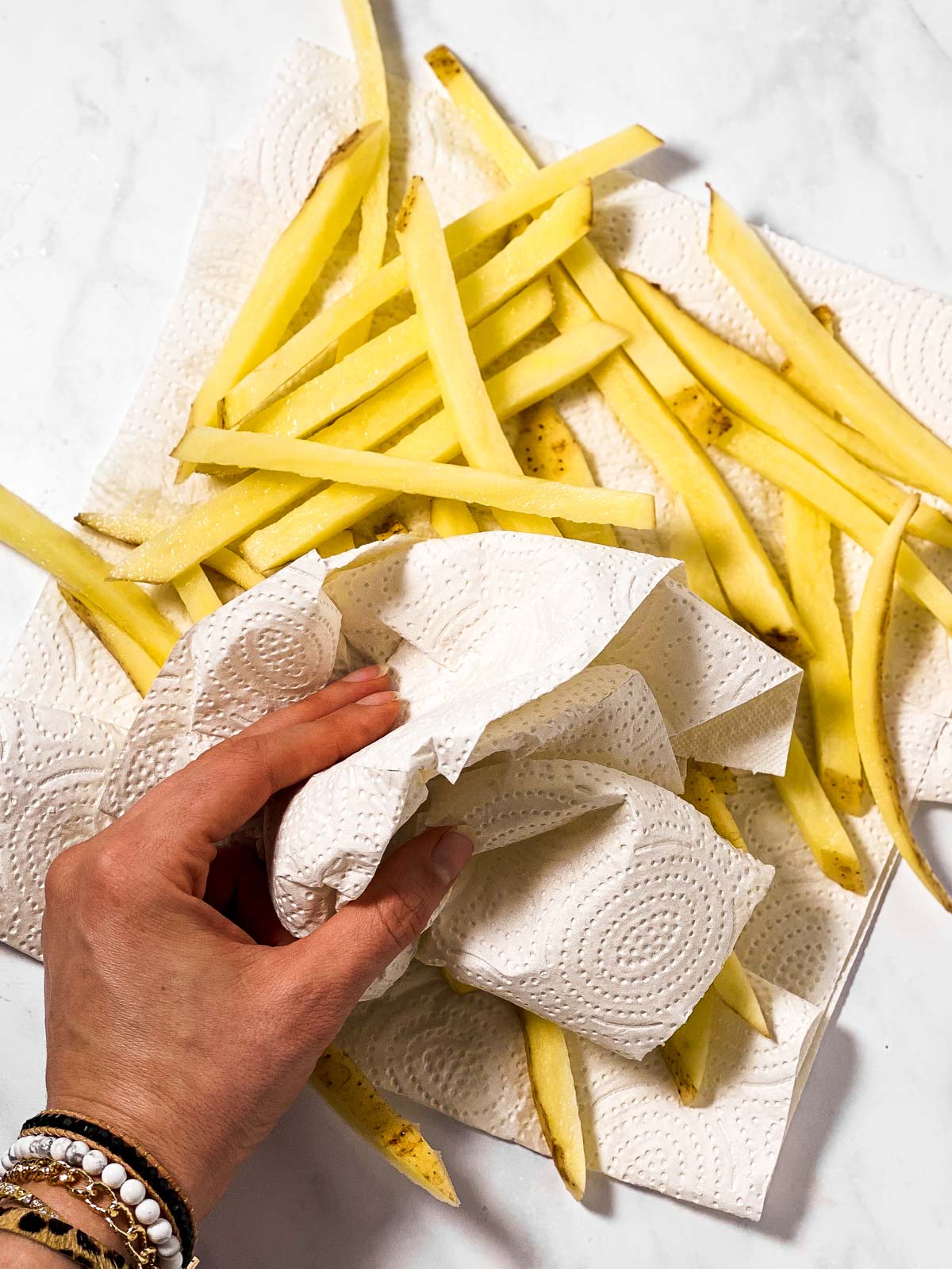 female hand using paper towels to dry uncooked french fries