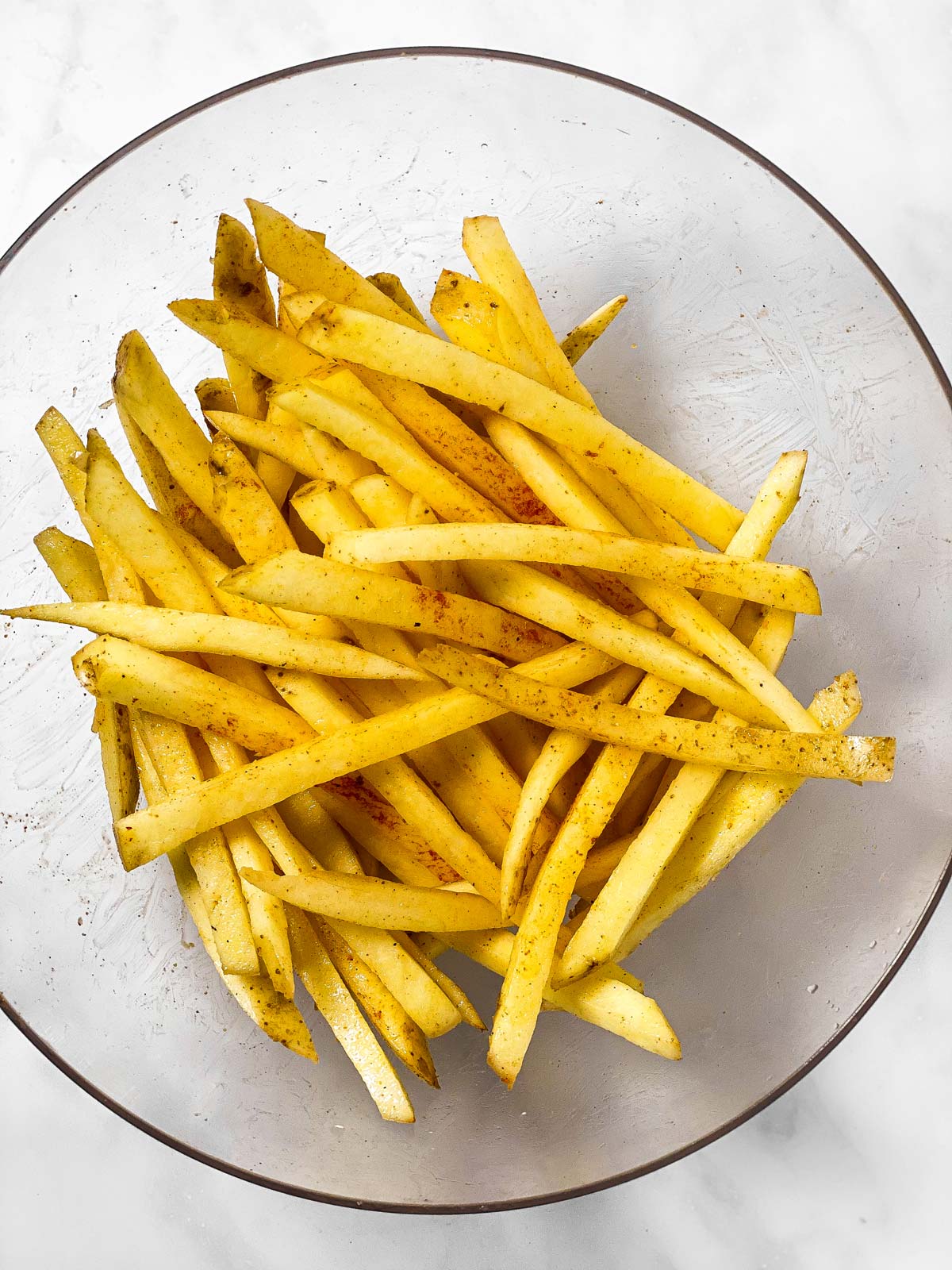 uncooked french fries in glass bowl covered in oil and seasoning