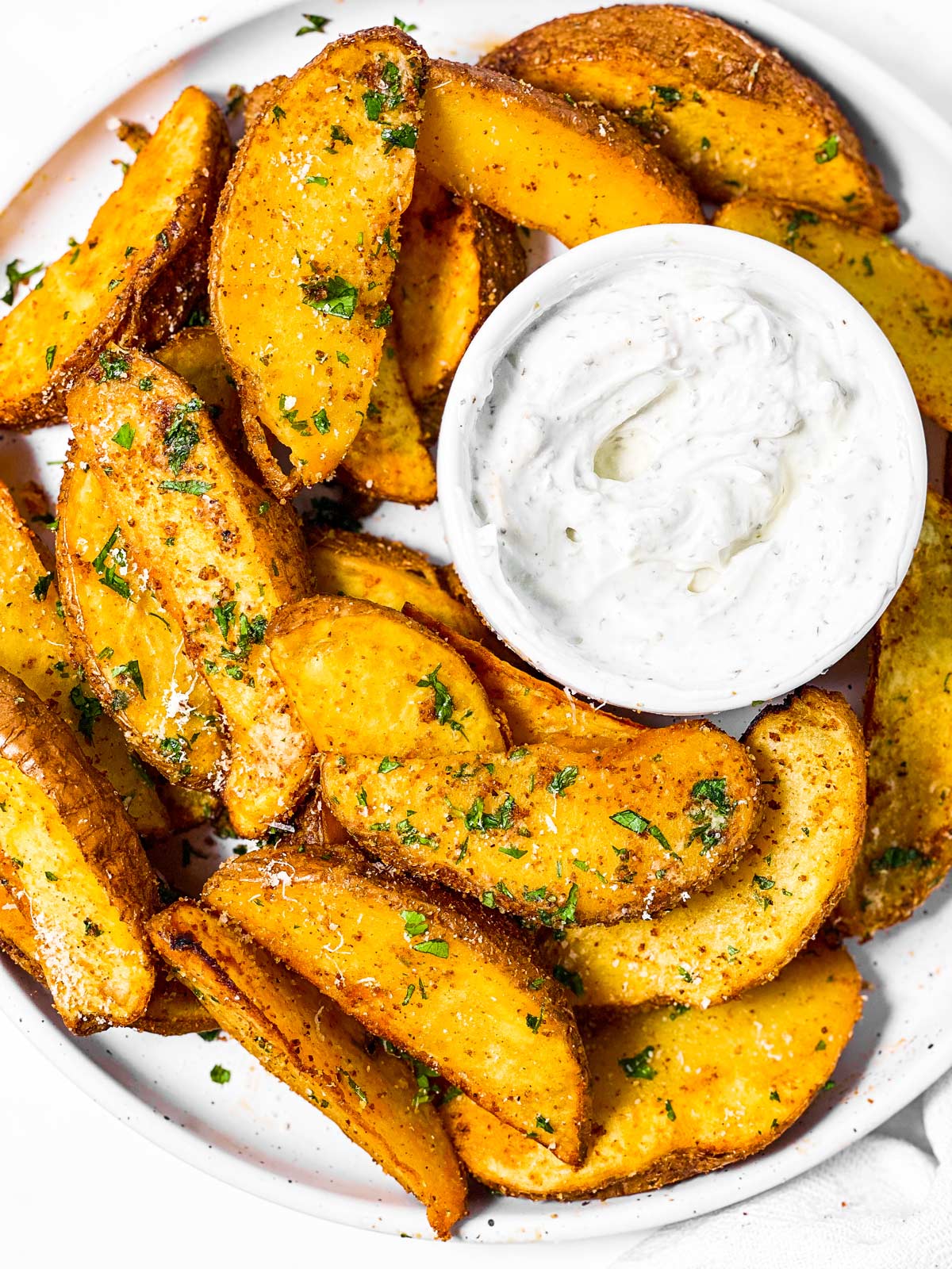 overhead view of air fryer potato wedges on plate with sour cream