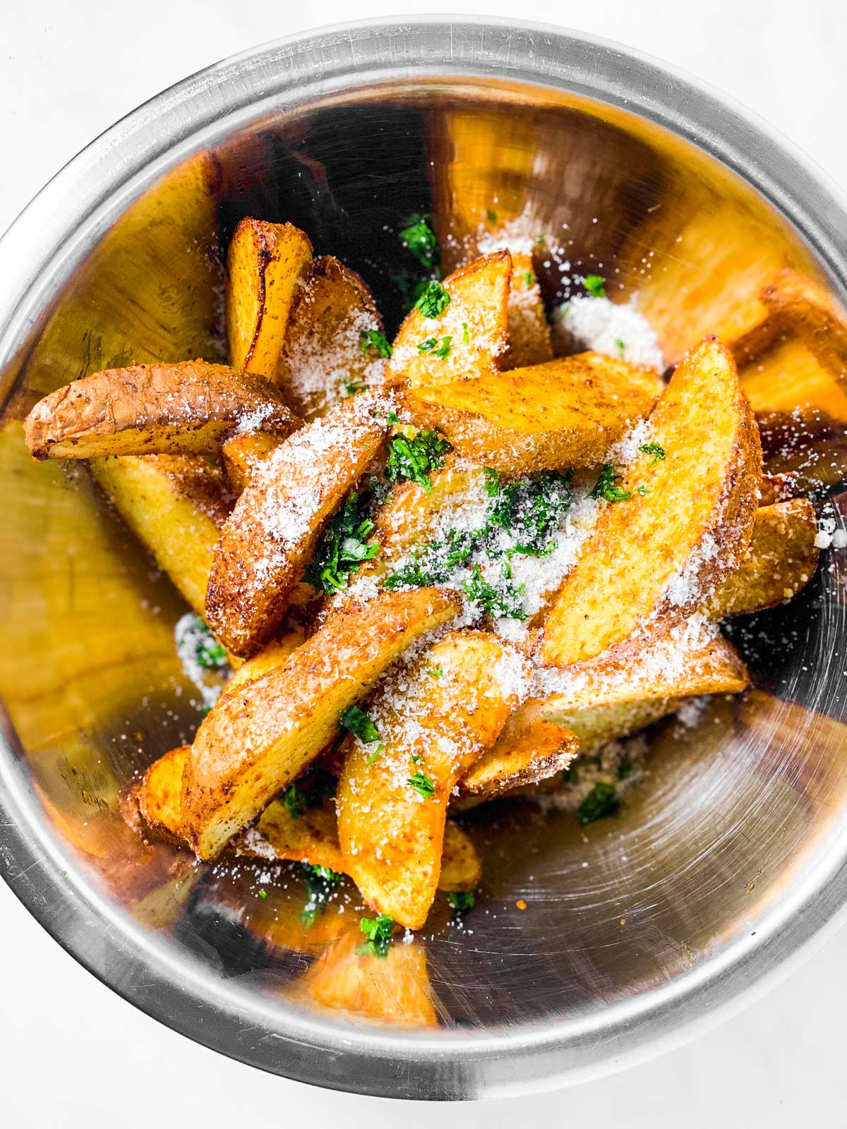 potato wedges in bowl with parmesan cheese and chopped parsley