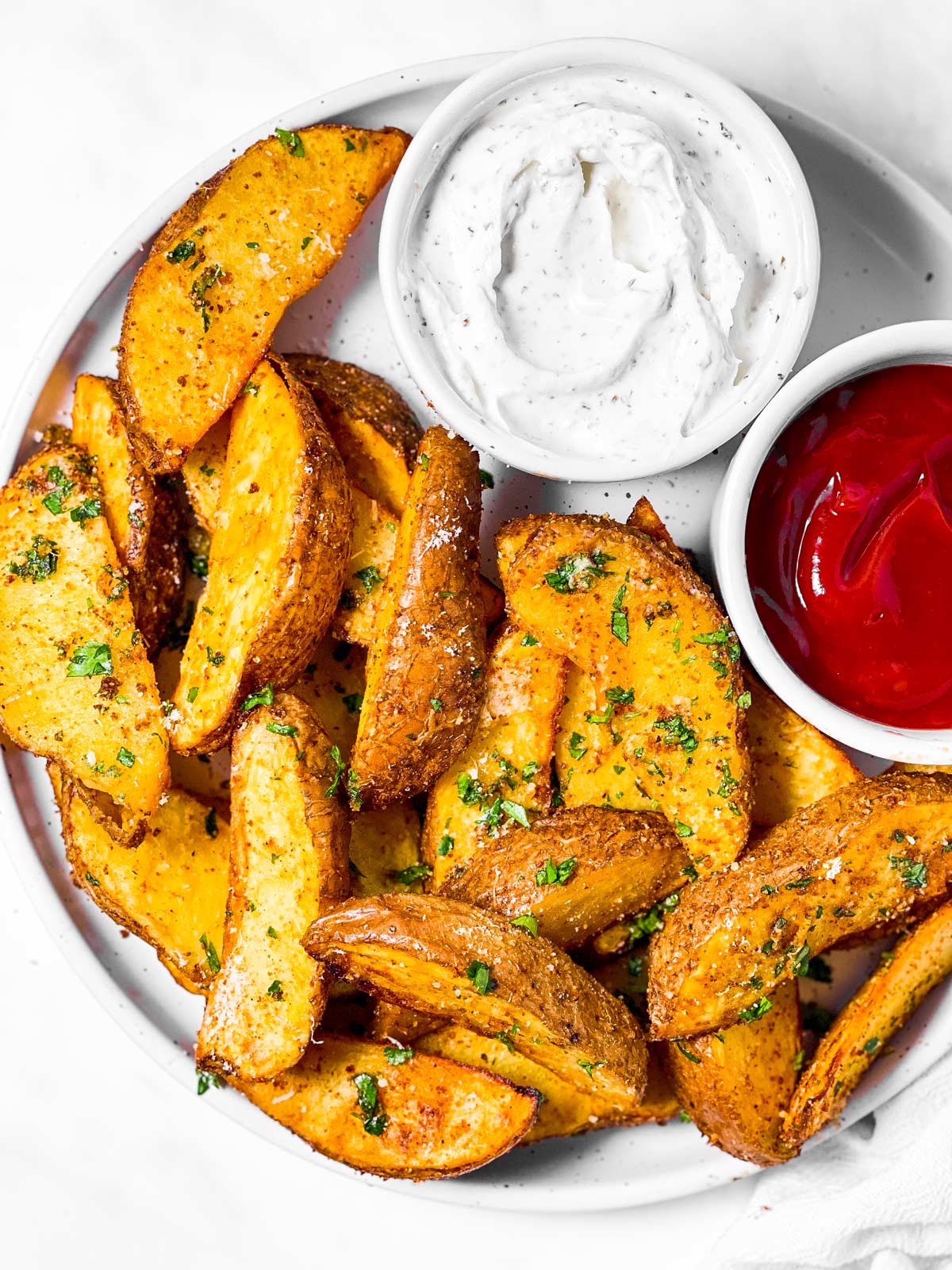 overhead view of air fryer potato wedges on plate with ketchup and sour cream