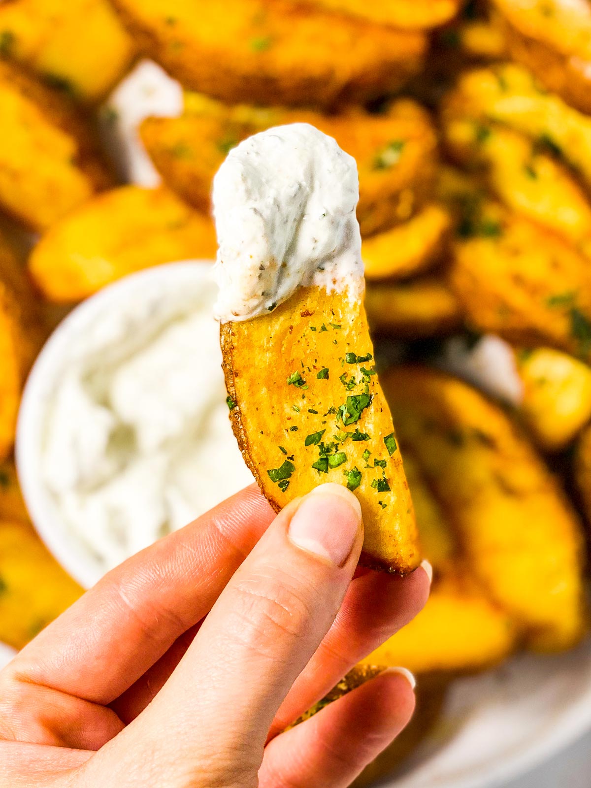 female hand holding a potato wedge covered with sour cream