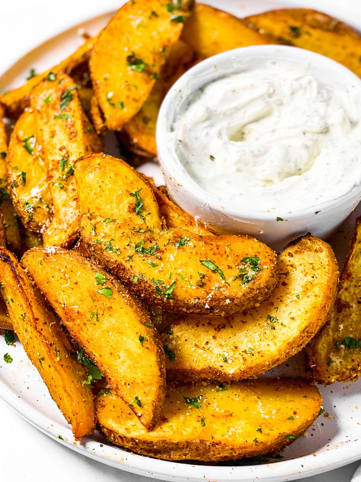 frontal view of potato wedges of plate with small bowl of sour cream