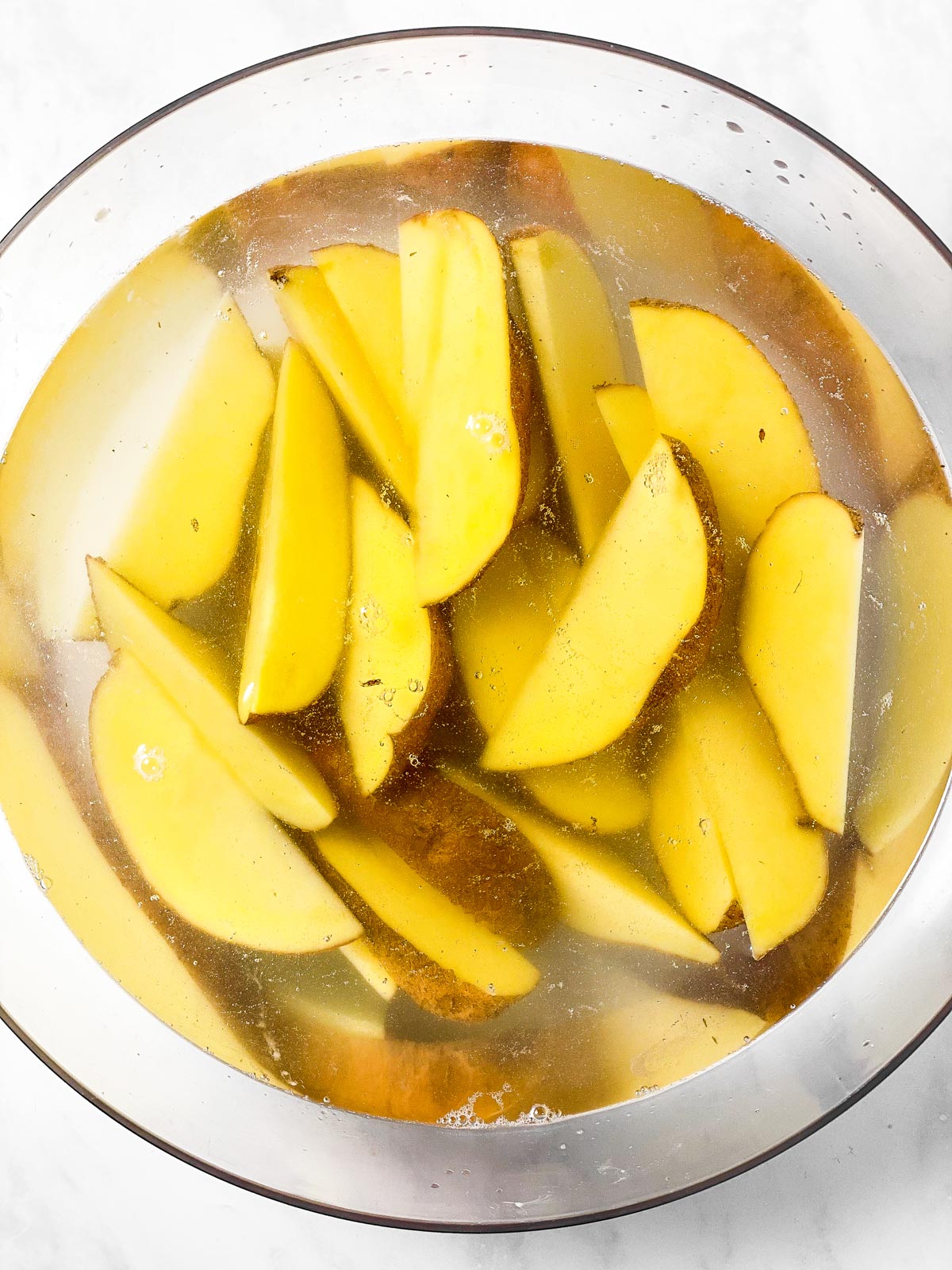 glass bowl filled with raw potato wedges and water