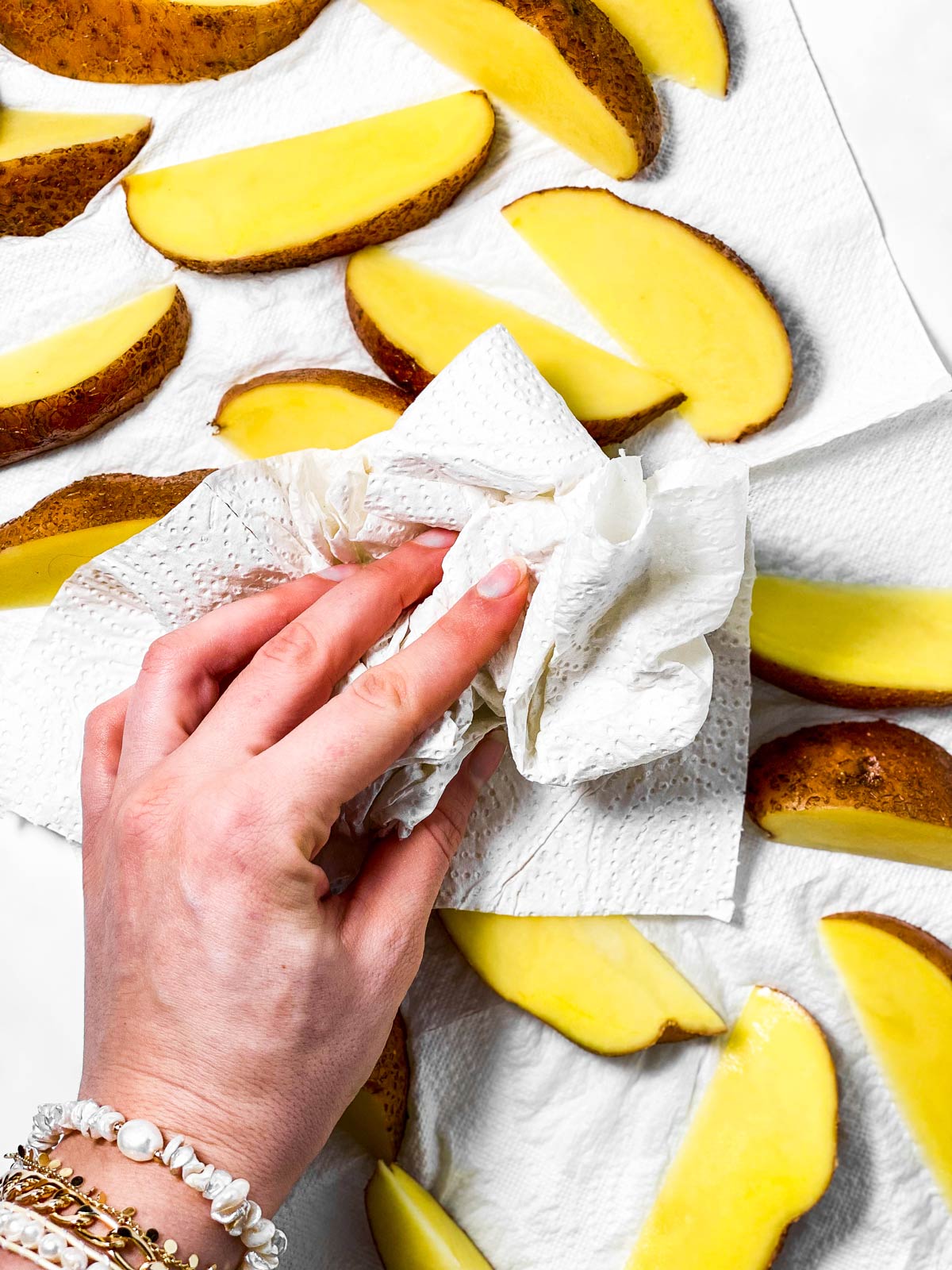 female hand patting dry potato wedges with paper towels