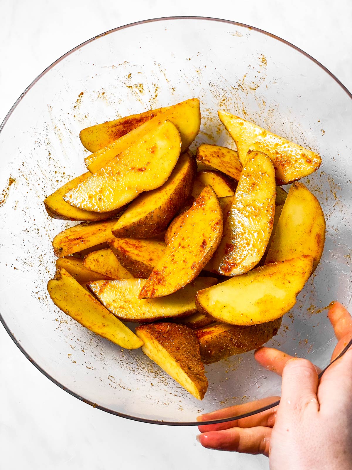 female hand holding glass bowl filled with seasoned potato wedges