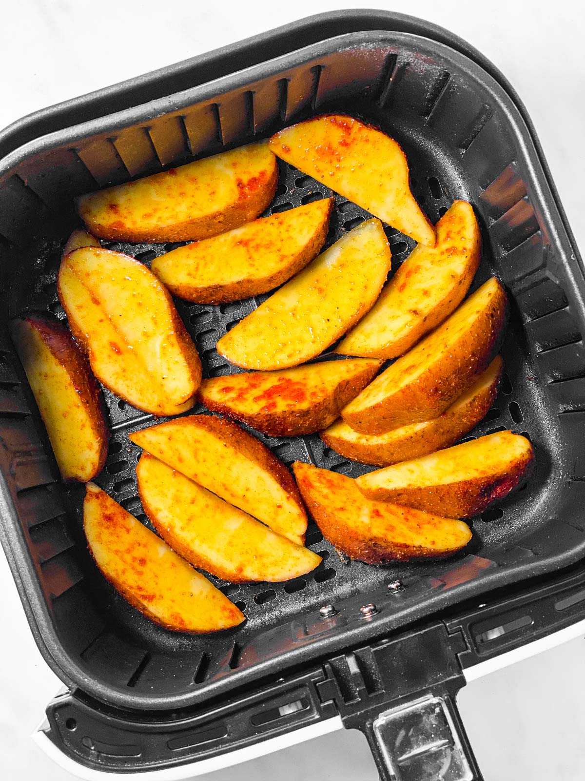 overhead view of raw potato wedges in air fryer basket