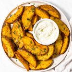 overhead view of air fryer potato wedges on plate with sour cream