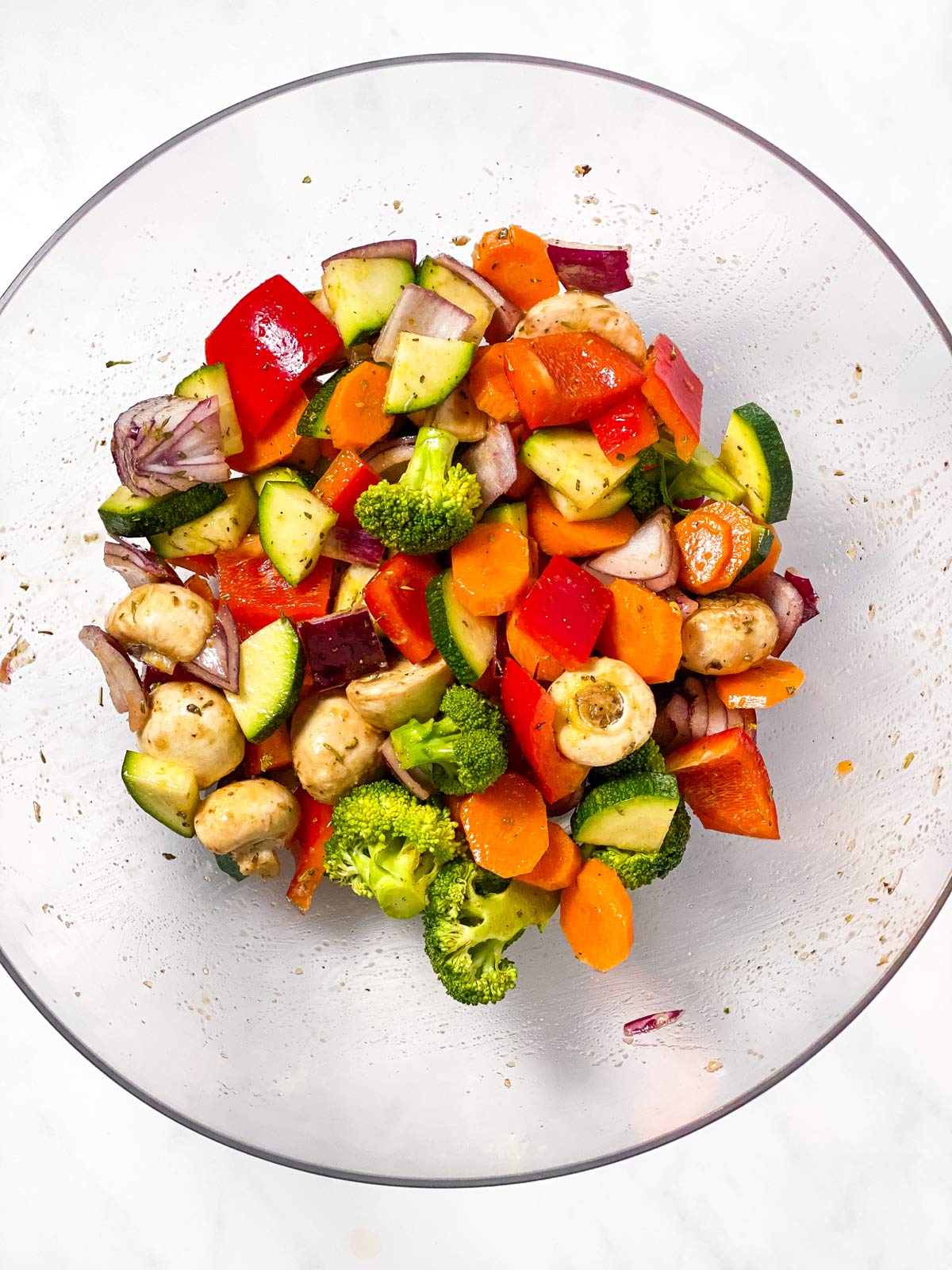 overhead view of chopped vegetables with oil and seasoning in large glass bowl