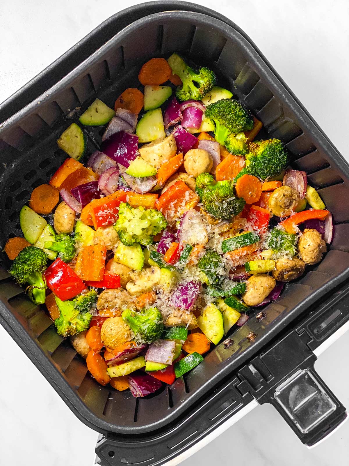 vegetables in air fryer basket sprinkled with grated parmesan cheese