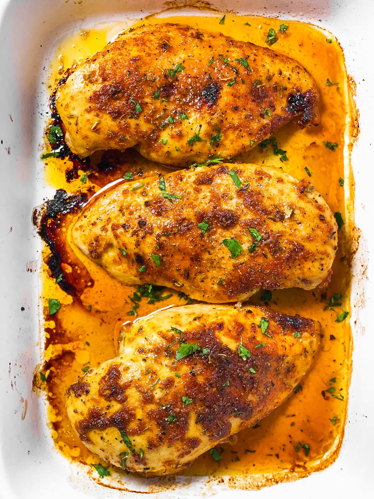 overhead close up view of three oven baked chicken breasts in white casserole dish