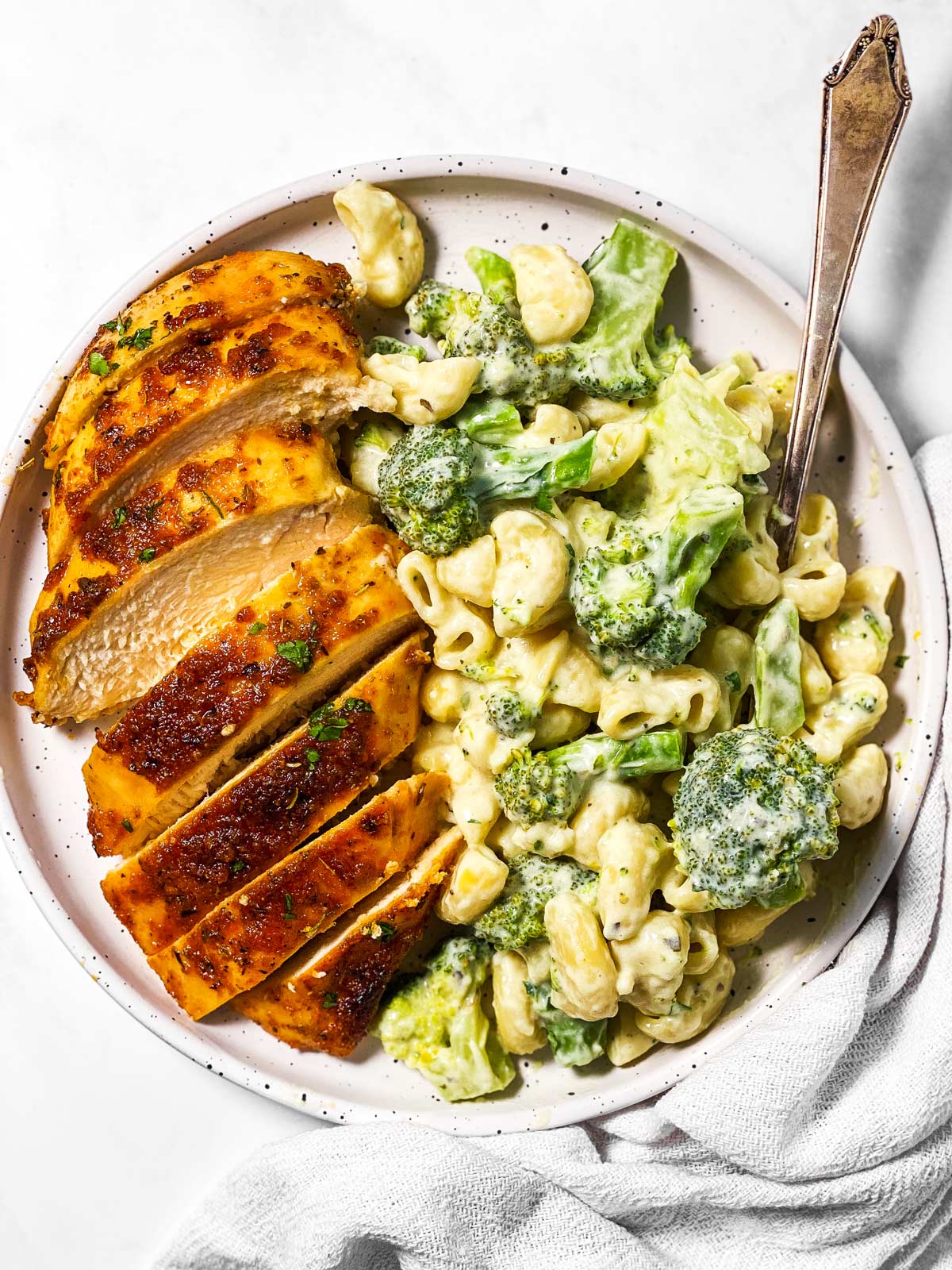 overhead view of sliced baked chicken breast and broccoli pasta on white plate