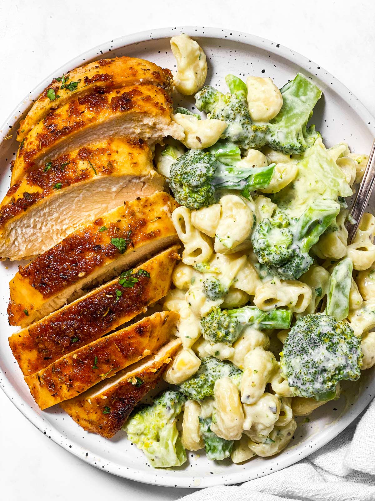 overhead view of sliced baked chicken breast and broccoli pasta on white plate