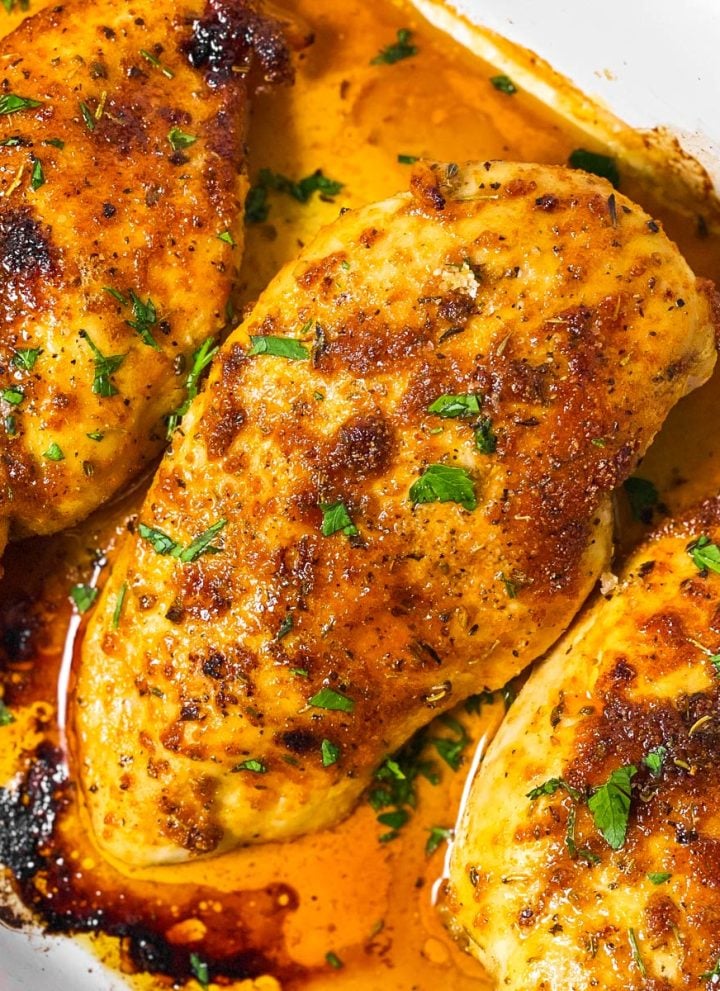 overhead view of three oven baked chicken breasts in white casserole dish