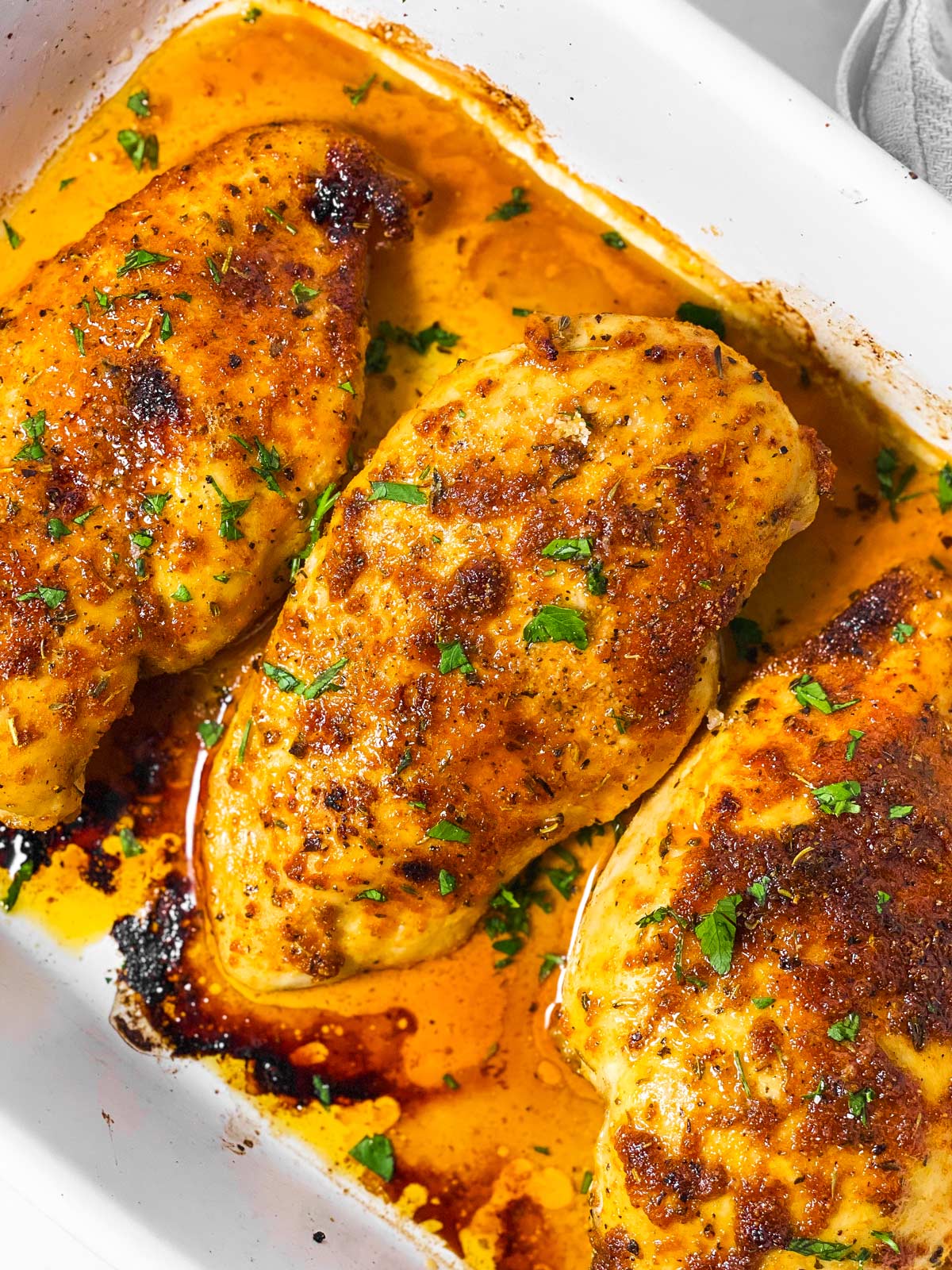 overhead view of three oven baked chicken breasts in white casserole dish