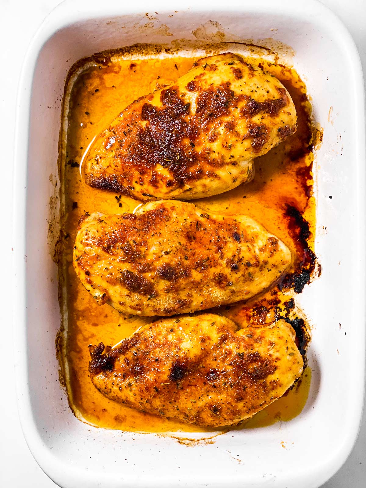 three seasoned, baked chicken breasts in white casserole dish