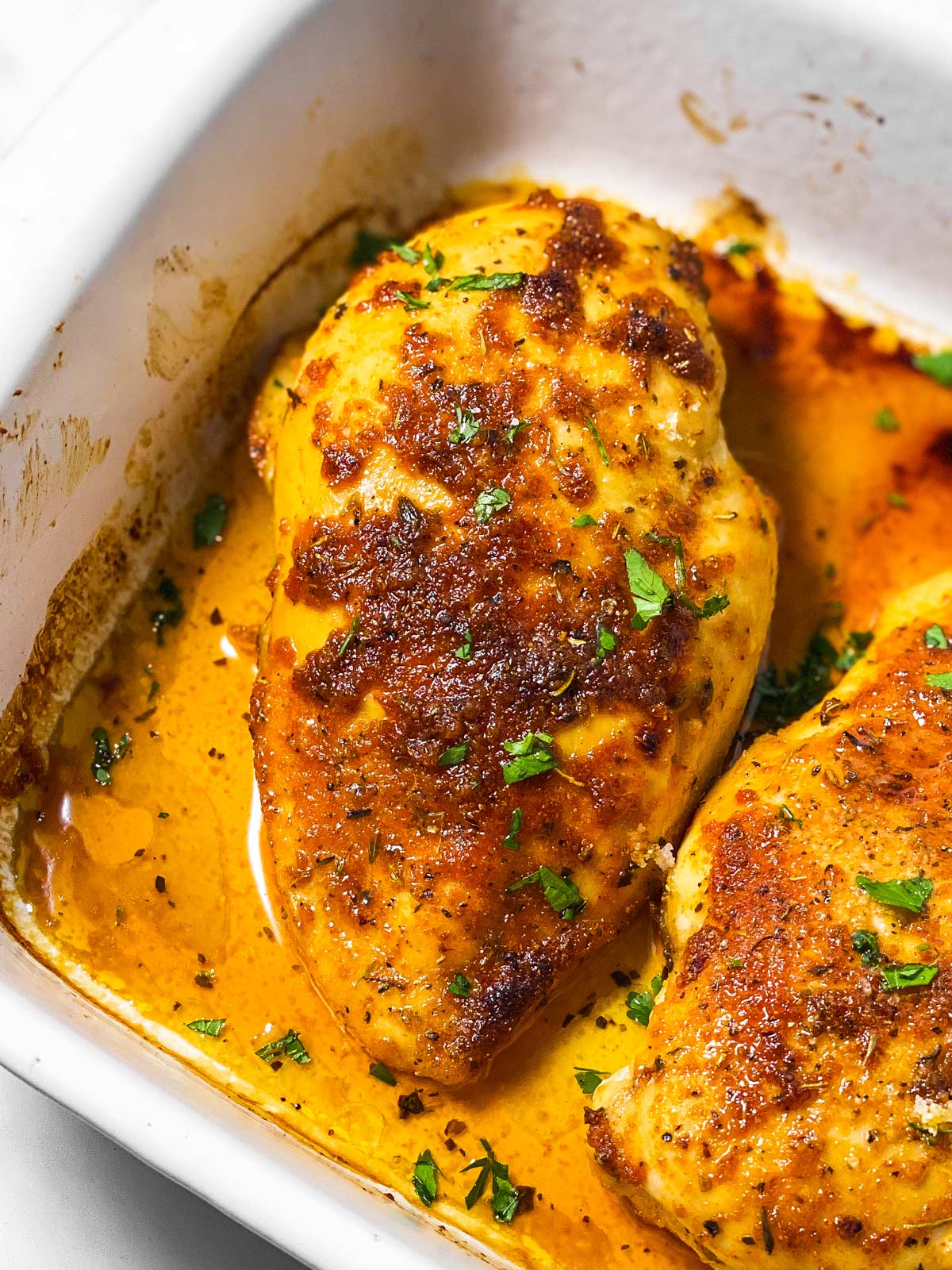 frontal view of baked chicken breast in white casserole dish