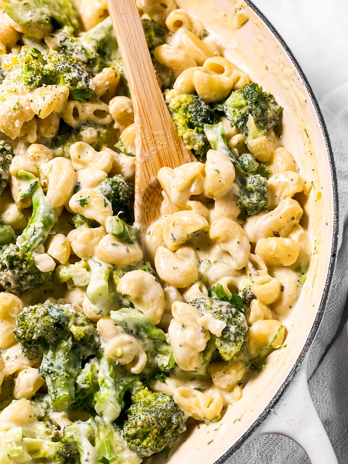 frontal close up view of wooden spoon in pot with creamy broccoli pasta